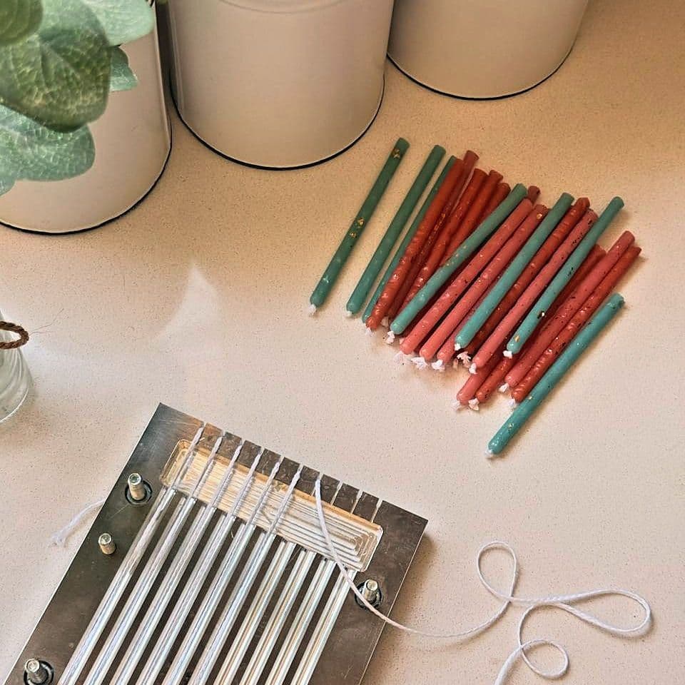 Hand-dipped candles drying on the table beside the wick frame